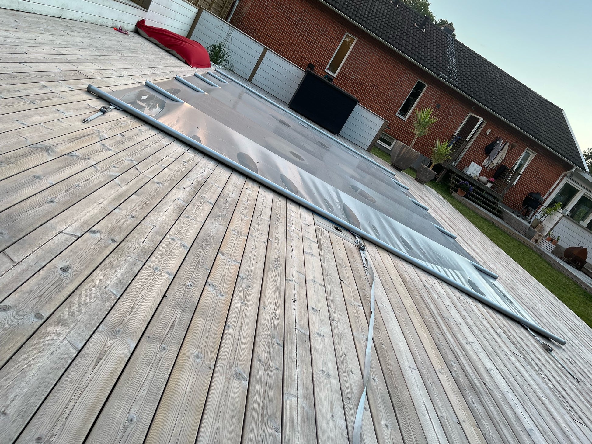 Grått Rib-Cover poolskydd utrullat på trädäck bredvid bostadshus